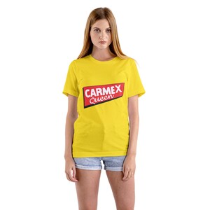 Könnte beinhalten: Ein gelbes T-Shirt mit einem roten und weißen Aufdruck, auf dem "CARMEX Queen" steht.