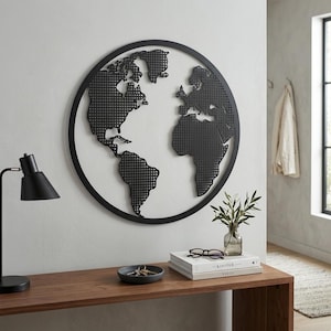 May include: A circular black metal wall art piece featuring a stylized world map with a grid-like perforated texture. The continents are depicted in a solid black silhouette within a thin circular frame, mounted on a plain light-colored wall.