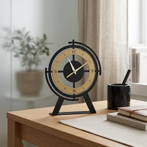 May include: A tabletop clock featuring a circular black frame with a gold-toned inner ring. The clock face displays black numerals at the 12, 3, 6, and 9 o'clock positions, with white hour and minute hands and a yellow second hand on a black center.