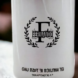 K&ouml;nnte beinhalten: Wei&szlig;e Flasche mit einem schwarzen Kranzdesign und dem Buchstaben F in der Mitte. Der Text "Fernando" befindet sich innerhalb des Kranzes. Der Text "GHU 1217 EI PEILTMH T6" befindet sich am Boden der Flasche.