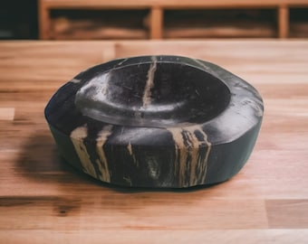 May include: A black and brown wooden bowl with a smooth, rounded interior. The bowl has a natural wood grain pattern and is made from a single piece of wood.
