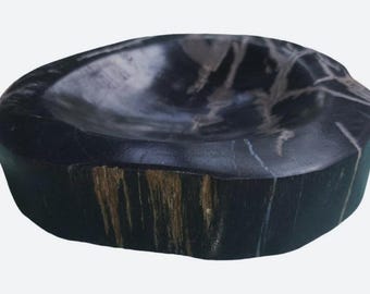 May include: A dark, polished stone bowl with a smooth, concave interior and a rough, textured exterior. The surface features natural white veining patterns against a deep black base, with visible brown wood-like grain details on the side.