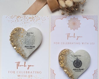 Puede incluir: Dos adornos de resina en forma de corazón con detalles de pan de oro sobre tarjetas blancas. Cada tarjeta incluye el texto Thank you FOR CELEBRATING WITH US!, los nombres Aysha & Moustafa y la fecha 01.01.2025. Un corazón muestra el texto Ayatul Kursi.