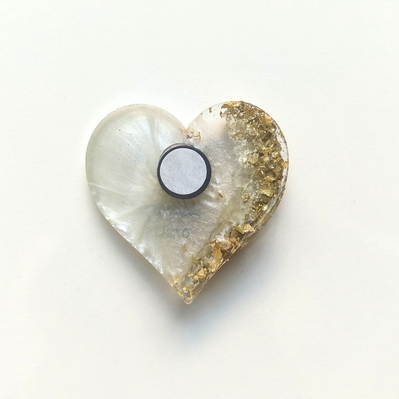 May include: White heart-shaped resin ornament with gold leaf accents and a black magnetic backing.