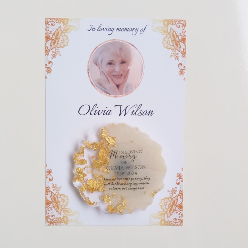 May include: A white memorial card with a gold border and a photo of a woman. The card reads "In loving memory of Olivia Wilson 1958-2024. These we love don't go away, they walk beside us every day, unseen, unheard, but always near."