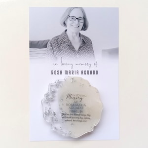May include: A white memorial plaque with silver glitter embedded in the resin. The plaque has a white background with black text that reads "In Loving Memory of Rosa Maria Aguado 1958-2024". The text continues with a quote: "Those we love don't go away, they walk beside us every day, unseen, unheard, but always near."