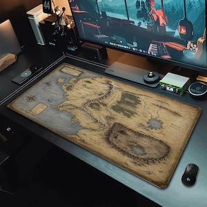 Può includere: Un tappetino da scrivania rettangolare con una mappa dettagliata della Terra di Mezzo in stile vintage. La mappa mostra regioni come Eriador, Rohan, Gondor e Mordor con caratteristiche geografiche etichettate, una rosa dei venti e una legenda.