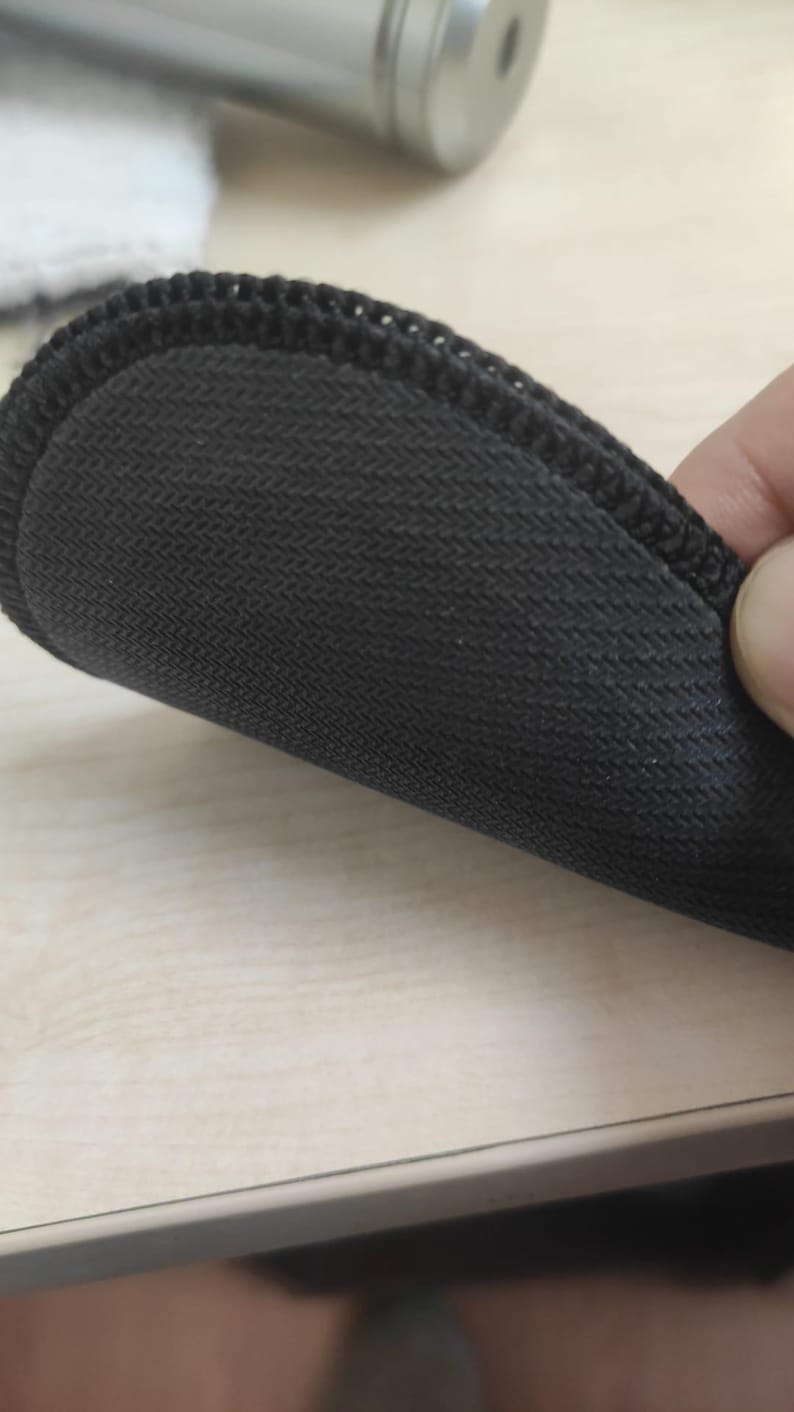 May include: A circular black coaster featuring a textured, non-slip rubber base with a distinct herringbone pattern. The edge of the coaster is finished with a durable, tightly stitched black fabric border that provides a clean, uniform appearance.