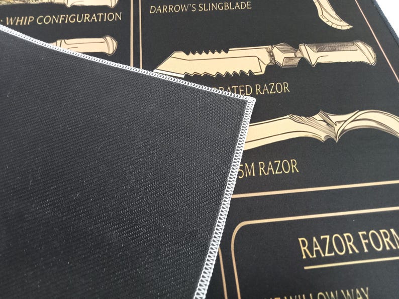May include: A black rectangular mat with a white stitched edge, featuring a graphic print of various bladed weapons in tan and gold. The text includes labels such as WHIP CONFIGURATION, DARROW'S SLINGBLADE, SERRATED RAZOR, SM RAZOR, and RAZOR FORM.