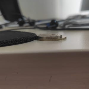 May include: Two circular metallic coins stacked on top of each other. The top coin is silver in color with a smooth edge, while the bottom coin is gold in color with a reeded edge. The coins are positioned horizontally on a flat surface.