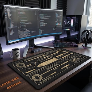 May include: A black desk mat featuring gold-colored technical illustrations of fictional weapons from the Red Rising series, including coiled razors, blades, and labeled diagrams, positioned on a wooden desk with a computer monitor and keyboard.