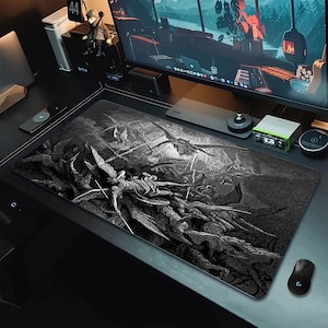 May include: A black and white desk mat with a detailed illustration of a battle scene with winged figures. The mat is rectangular and designed to protect the desk surface while providing a smooth surface for a mouse.