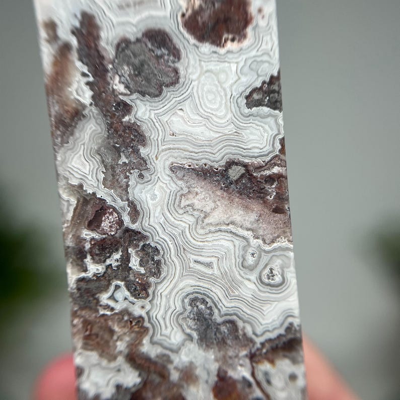 May include: Close-up of a polished stone with a unique pattern. The stone features a mix of colors, including white, gray, and brown, with intricate, swirling lines and patterns. The surface is smooth and reflective, highlighting the natural beauty of the stone.