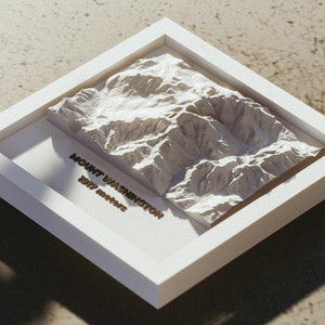 May include: A white framed 3D relief map of Mount Washington, with the text "MOUNT WASHINGTON 1917 meters" in gold lettering. The map is a detailed representation of the mountain's terrain.