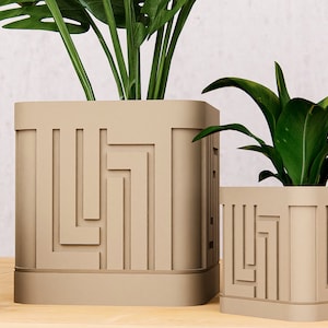 May include: Three square beige planters of varying sizes, each featuring a raised geometric pattern of vertical and horizontal lines on the exterior. Each planter holds a green plant with broad or pointed leaves, creating a cohesive set.
