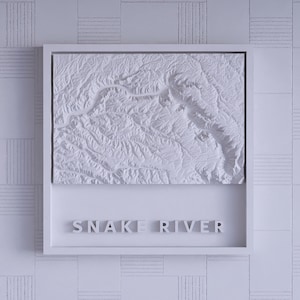 May include: A white framed relief map of the Snake River. The map is a detailed 3D representation of the river's topography, with the river's name in block letters below the map.