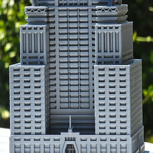 May include: A gray 3D printed model of a skyscraper with a detailed facade and a small entrance at the base.