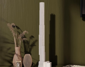 Op de afbeelding: Een wit model van een hoog wolkenkrabbergebouw met een bruine rieten vaas en een geweven draadmand op een groene ondergrond.