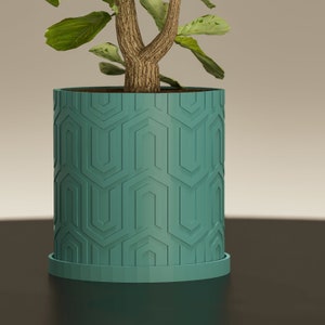 Op de afbeelding: Een teal plantenpot met een geometrisch patroon, met een groene, bladerrijke plant erin.