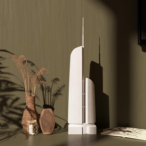 May include: A white model of a skyscraper with a brown wicker vase and dried flowers on a brown surface.