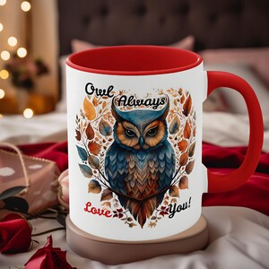 May include: A white ceramic mug with a red interior and handle. The mug features a detailed illustration of an owl surrounded by leaves, with the words "Owl Always Love You!" in black script. The owl is primarily blue and brown.