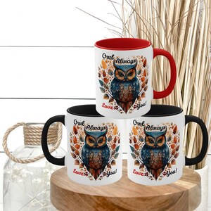 May include: White ceramic mugs with a colorful owl design. The owl is depicted with blue, brown, and orange feathers, surrounded by autumn leaves. The mugs have black and red handles and the text "Owl Always Love You!"