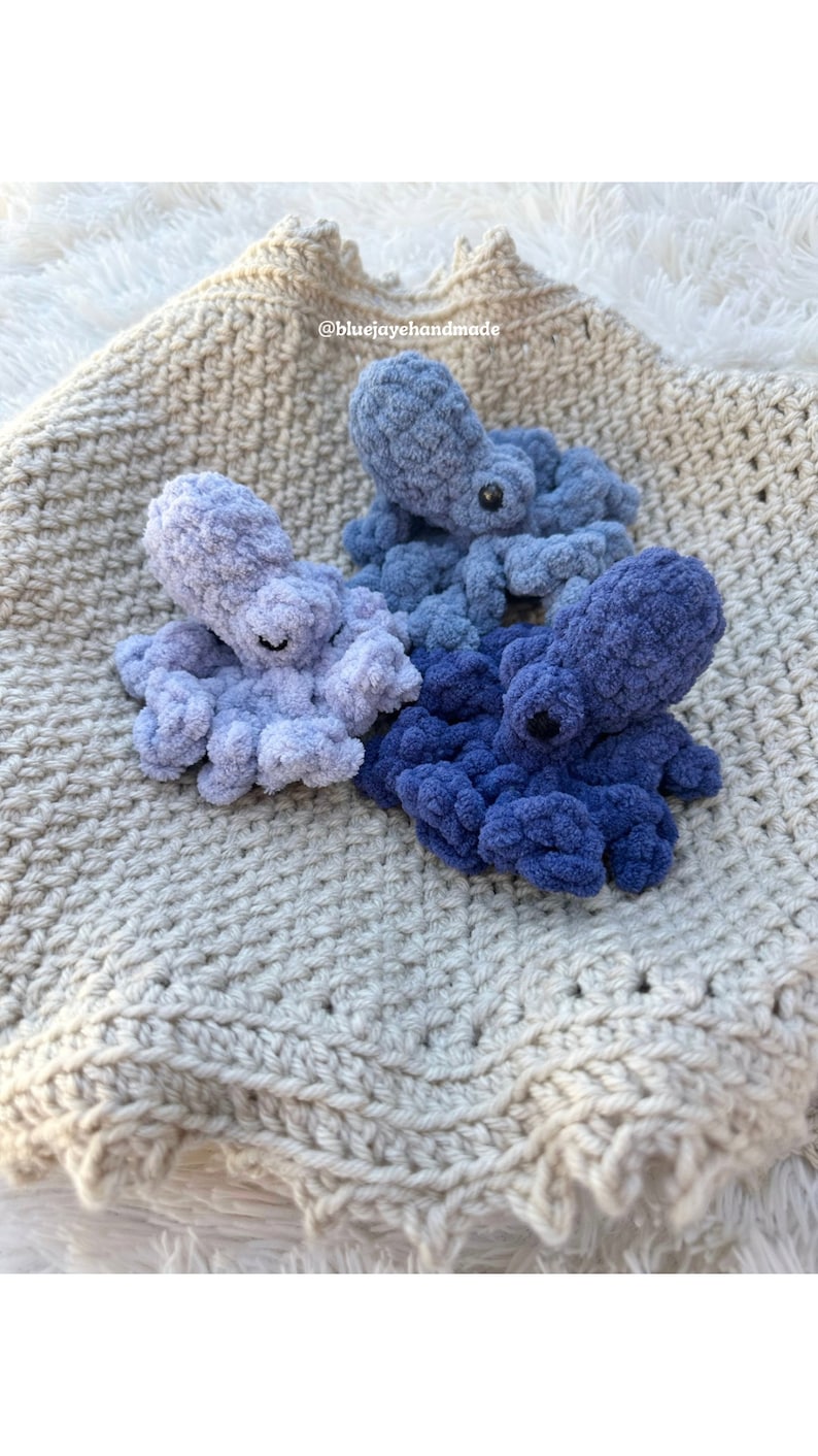 Puede incluir: Tres peluches de pulpo tejidos a crochet en tonos de azul, azul claro y morado, descansando sobre una manta de crochet beige. La manta tiene un borde con flecos. El texto "@bluejayehhandmade" es visible en la esquina superior derecha de la imagen.