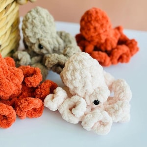 Puede incluir: Tres peluches de pulpo de crochet en diferentes colores: beige, naranja y rosa. Las peluches tienen ojos negros y est&aacute;n hechas con un hilo suave y peludo.