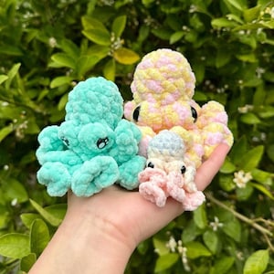 Puede incluir: Tres peluches de pulpo de crochet en diferentes colores: azul verdoso, rosa y amarillo con lunares blancos. Los peluches est&aacute;n en la mano de una persona.