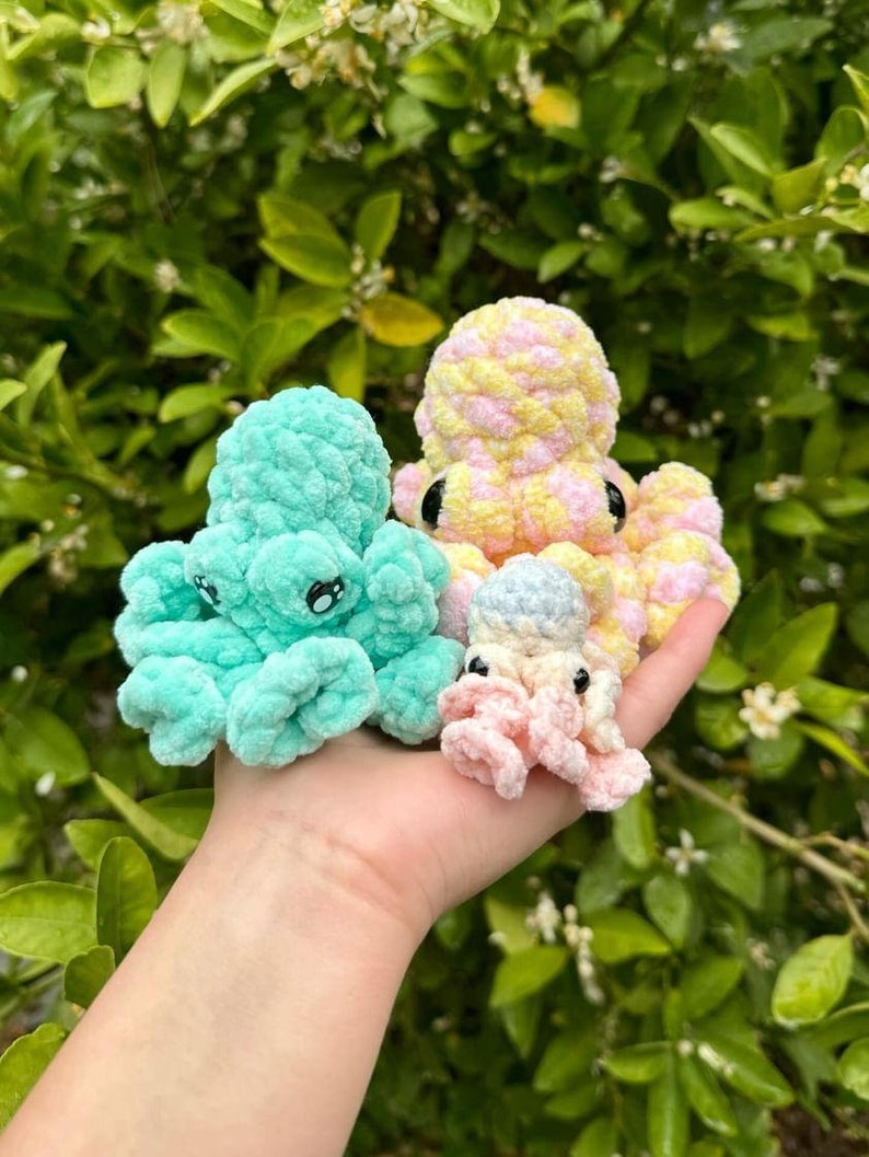 Puede incluir: Tres peluches de pulpo de crochet en diferentes colores: azul verdoso, rosa y amarillo con lunares blancos. Los peluches est&aacute;n en la mano de una persona.