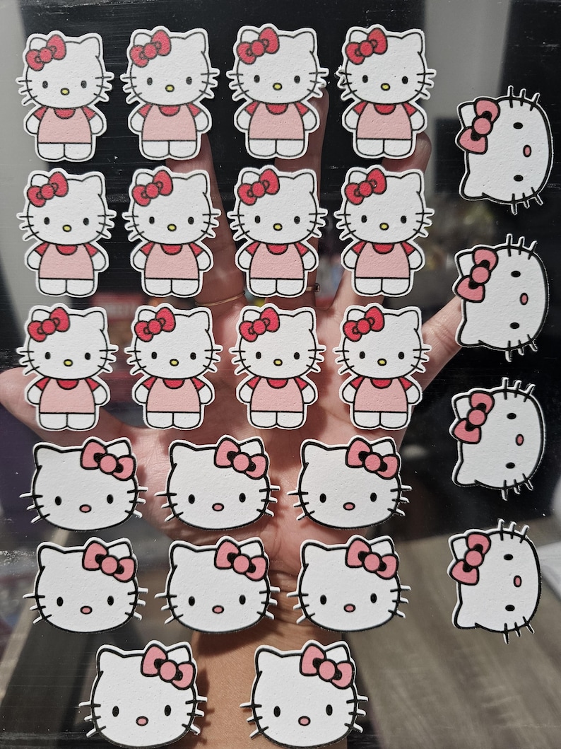 May include: A collection of Hello Kitty stickers. The stickers feature the iconic cartoon cat in a pink dress and bow. Some stickers are just the cat's face with a bow. The stickers are white, pink, and black.