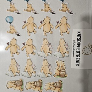 May include: A sheet of Winnie the Pooh stickers. The stickers feature Pooh Bear in various poses, including holding a blue balloon, sitting on a cloud, and with a honey pot. The stickers are tan, with accents of blue, pink, and brown.