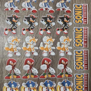 May include: A collection of stickers featuring Sonic the Hedgehog characters including Sonic, Shadow, Tails, and Knuckles, along with four vertical stickers displaying the text Sonic The Hedgehog in blue, yellow, and red lettering.