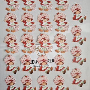 May include: A selection of Strawberry Shortcake character stickers. The stickers depict the character in a red dress, a pink hat, and green and white striped leggings. Some stickers include a small pink pig. The text "CDIP REA" is visible.
