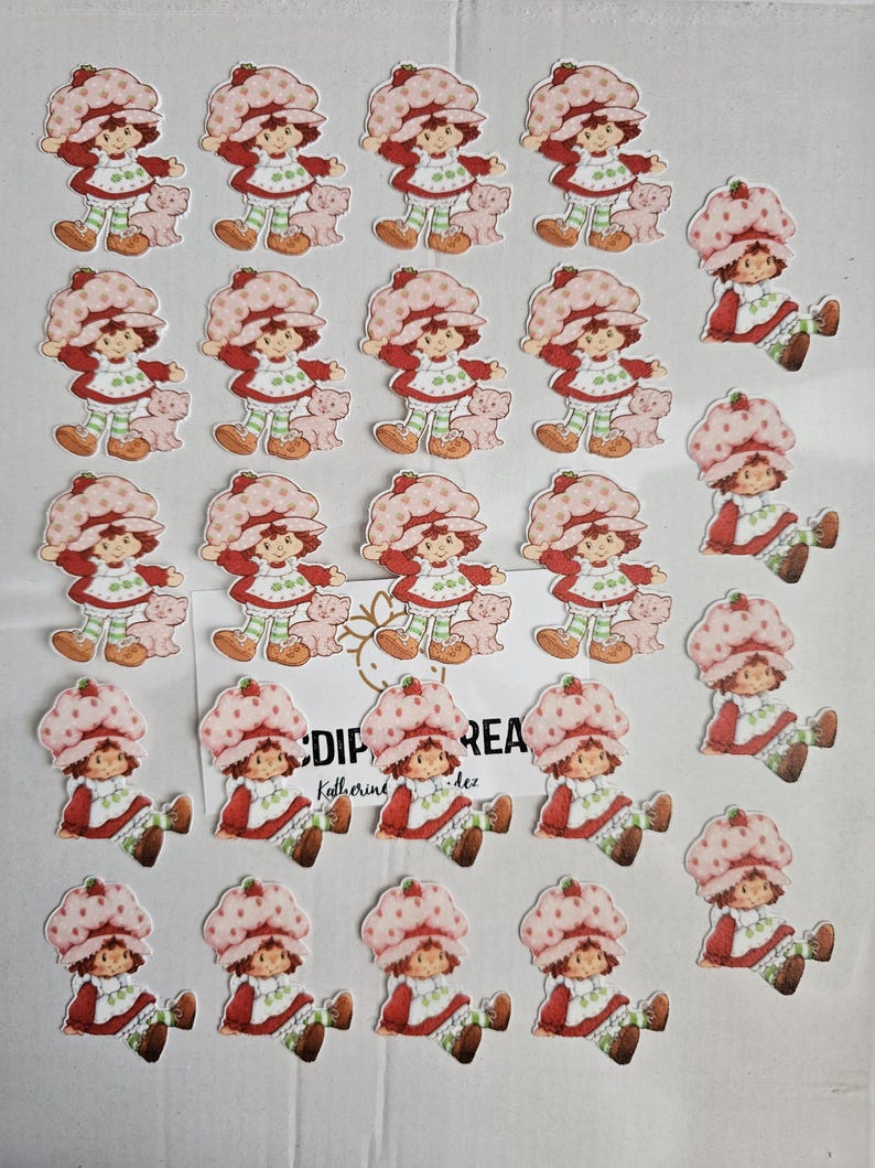 May include: A selection of Strawberry Shortcake character stickers. The stickers depict the character in a red dress, a pink hat, and green and white striped leggings. Some stickers include a small pink pig. The text "CDIP REA" is visible.