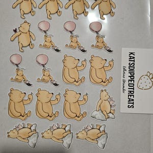 May include: A collection of Winnie the Pooh themed stickers. The stickers feature the bear in various poses, including holding a heart, a balloon, and sitting on a cloud. A small card with the text "KATSDIPPEDTREATS" is also visible.