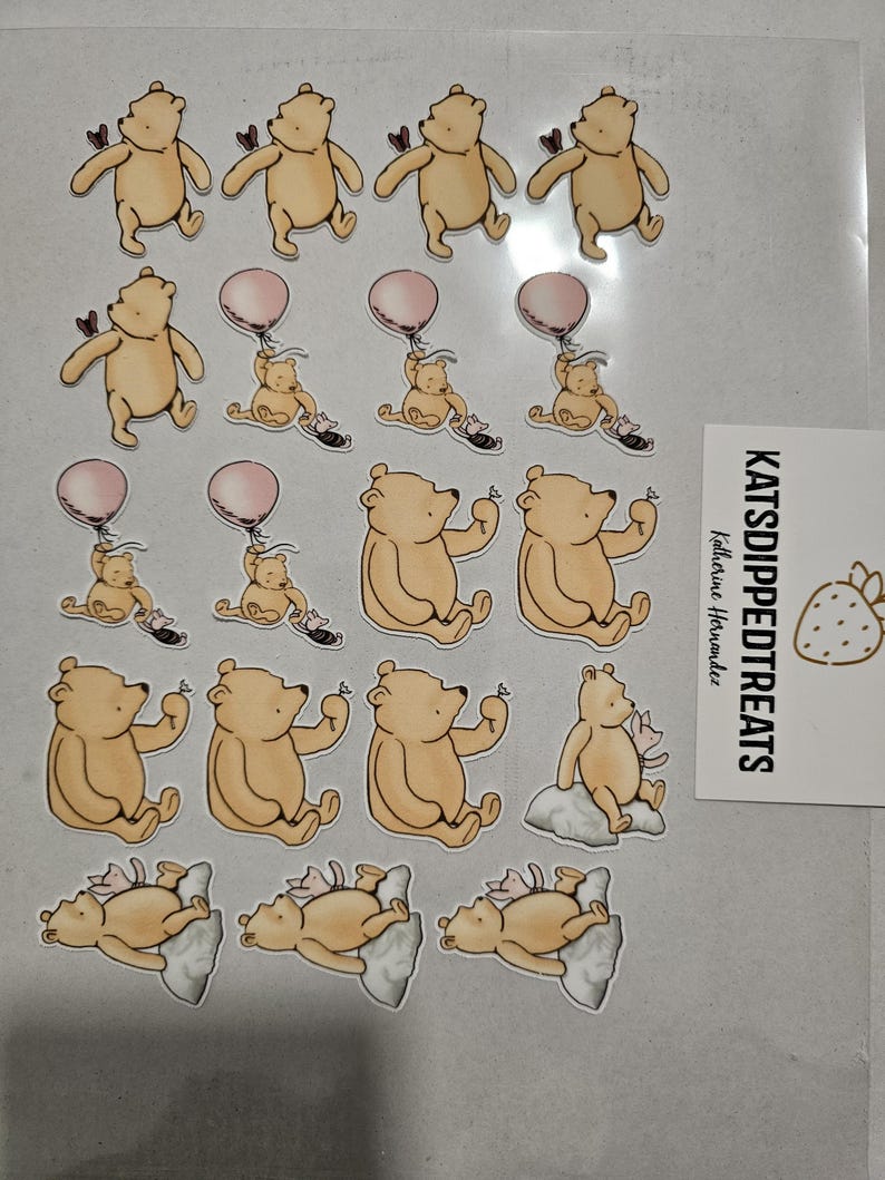 May include: A collection of Winnie the Pooh themed stickers. The stickers feature the bear in various poses, including holding a heart, a balloon, and sitting on a cloud. A small card with the text "KATSDIPPEDTREATS" is also visible.