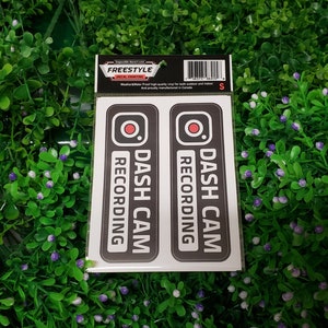 Puede incluir: Dos pegatinas blancas y negras con el texto "DASH CAM RECORDING" y un círculo rojo con un icono de cámara. Las pegatinas están sobre un fondo blanco.