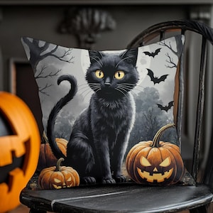 May include: Halloween-themed decorative pillow featuring a black cat with yellow eyes, sitting in front of a spooky forest scene with bats and pumpkins. The pillow is placed on a black wooden chair, with carved pumpkins in the background.