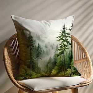 May include: A white throw pillow with a watercolor print of a misty forest scene. The pillow is sitting on a wicker chair.