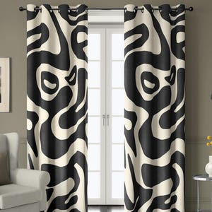 May include: A pair of decorative window curtains with a bold, abstract pattern. The design features large, flowing black shapes against a cream-colored background. The curtains are hung on a black rod, adding a modern touch to the room.