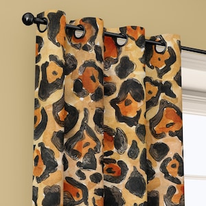 May include: A pair of leopard print curtains with a black curtain rod. The curtains feature a watercolor design with black and brown spots on a tan background. The curtains are hanging in front of a window.