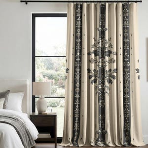 May include: Cream-colored bedroom curtains with a black floral and striped design. The curtains are hanging in front of a window, with a bed and nightstand visible in the room. The curtains have a classic, elegant style.