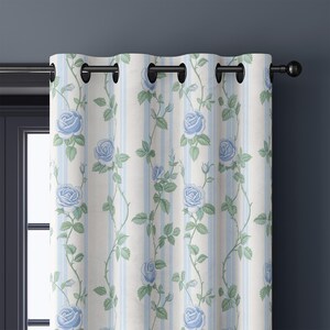 May include: A curtain panel featuring a vertical striped pattern in white and light blue, adorned with a repeating floral print of light blue roses and green leaves. The curtain is suspended from a black metal rod using black grommets.