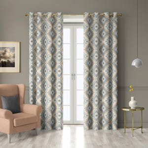 May include: Two patterned curtains with a geometric design in shades of gray, beige, and white hang from a gold rod. The curtains frame a white double door. A peach armchair and side table are in the foreground.