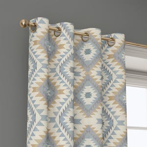 May include: A patterned curtain with a geometric design in shades of blue, beige, and gray. The curtain is hanging from a gold-colored rod with matching grommets. The design features diamond and triangle shapes.