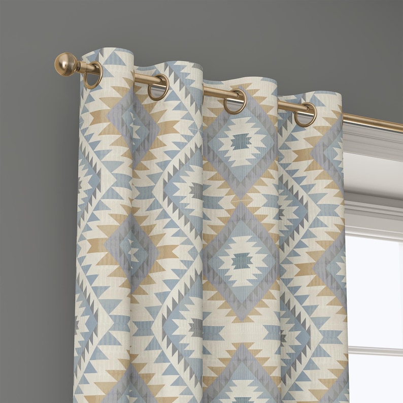 May include: A patterned curtain with a geometric design in shades of blue, beige, and gray. The curtain is hanging from a gold-colored rod with matching grommets. The design features diamond and triangle shapes.