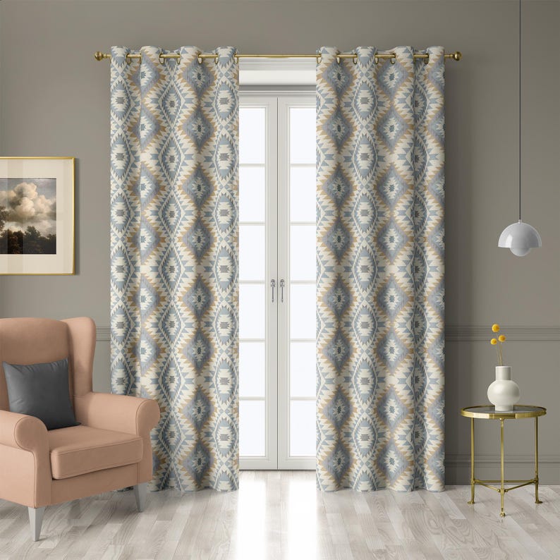 May include: Two patterned curtains with a geometric design in shades of gray, beige, and white hang from a gold rod. The curtains frame a white double door. A peach armchair and side table are in the foreground.