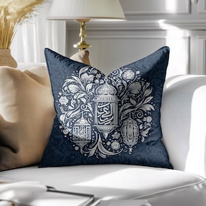May include: A navy blue decorative pillow with a white floral and lantern design. The pillow features a detailed pattern of leaves, flowers, and three ornate lanterns. The central lantern has Arabic script. The pillow is on a white couch.