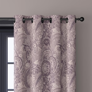 May include: A paisley patterned curtain in shades of purple and cream hangs from a black rod. The curtain features a detailed floral design with a repeating pattern. The grommets are black and the curtain is partially covering a dark blue window frame.